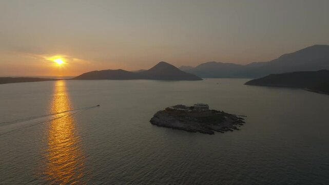 Cinematic drone view of Mamula Island with its stone fortress hotel against the backdrop of the sunset reflecting in the Adriatic Sea and the silhouettes of mountains, Montenegro, Europe