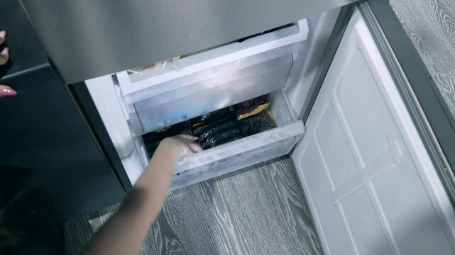 A girl takes frozen berries out of the freezer. Seasonal freezing of currant berries. Storage of vegetables and fruits. The concept of fast cooking of berries, fruits and vegetables.