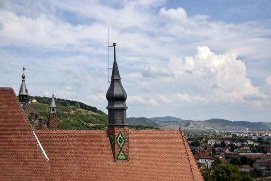 Stylized ventilation tower with lightning rod, installed on old red tiled roof of European town. Against background of bright blue expressive sky with fluffy clouds. Copy space for text.