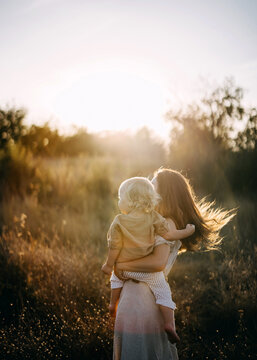 A mother carries her child in a sunlit field, in golden sunset light