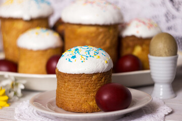 Easter bread with icing and yellow-blue sprinkles on a table with Easter eggs and spring flowers. Food for Easter