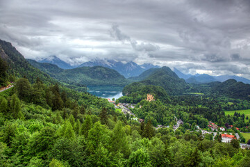 Fototapeta premium view of a castle in the mountains and a lake in bavaria germany. A mountain range with a lake in the middle. The lake is surrounded by trees. The mountains are covered in snow