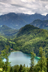 Fototapeta premium A alps mountain range in Germany with a alat lake in the foreground. The lake is surrounded by trees and mountains. The sky is cloudy and the mountains are covered in snow