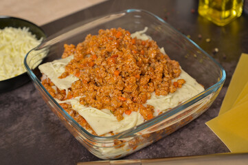Bolognese and béchamel sauces in a glass form. Lasagne pasta sheets. Grated cheese in a black bowl. Black background. Homemade lasagna cooking preparation