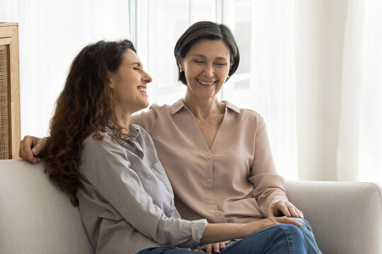 Family conversation. Happy loving mid aged mother young adult daughter relax on couch hug share smiles laughter enjoy talk feel moment of bonding closeness emotional connection between two generations