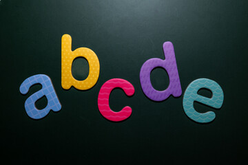 Colorful foam letters “a,” “b,” “c,” “d,” and “e” arranged on a dark background, symbolizing early learning, literacy, and creative design. Perfect for educational or childcare materials.