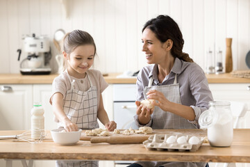 Noses in flour. Happy laughing young mom playing chefs at home kitchen with little daughter having fun cooking dumplings from homemade dough learn family recipe in form of game prepare dinner together
