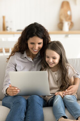Fototapeta premium Fun and studying with notebook. Happy two generation family young single mom small child daughter engaged in using interactive app on laptop enjoy game explore digital world with online learning tools