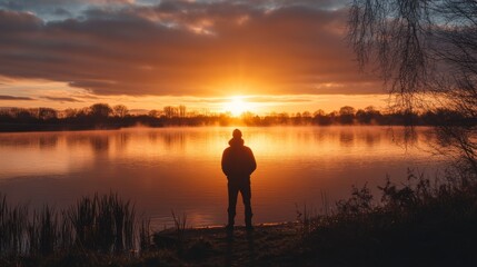 Silhouette of a Person at Sunset by a Calm Lake