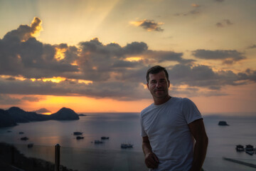 Fototapeta premium A man stands proudly against a stunning sunset backdrop, with numerous boats dotting the calm sea, beautifully capturing a moment of pure tranquility and peace, Komodo, Indonesia