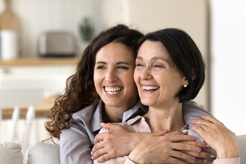 Support and love. Portrait happy millennial daughter hugging shoulders of mature mother staring at...
