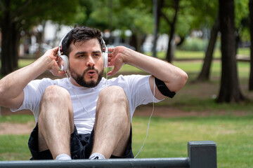 Hombre concentrado entrenando en el parque, haciendo abdominales mientras escucha música	