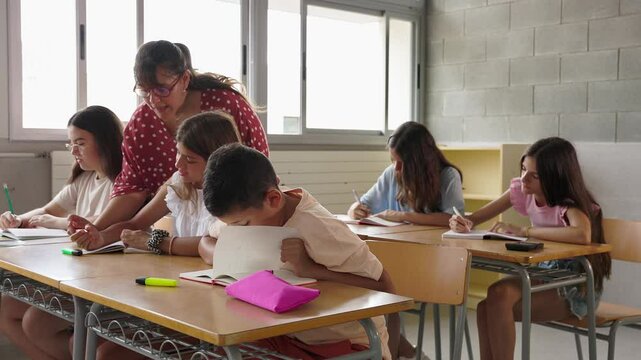 Young female teacher assisting elementary student girl during lesson in classroom at primary school. Education concept.