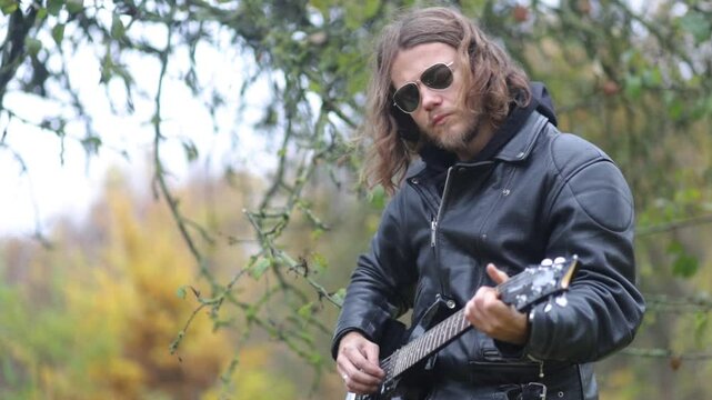man plays electric guitar gloomily outdoors in cloudy weather