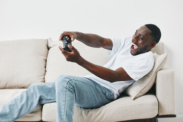 Excited young Black man playing video games on a sofa, showcasing joy and engagement in a modern...