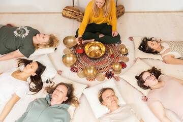 Group therapy session with Tibetan singing bowls for group of women lying on wooden floor...