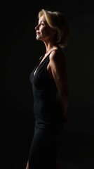 Fototapeta premium Elegant woman in black dress striking a confident pose in low lighting
