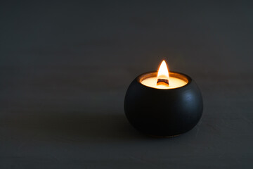 A white candle burns in a black plaster cup against a soft gray background, creating a calm and elegant atmosphere. Perfect for relaxation, meditation, or minimalist design themes.
