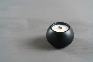 A white candle in a black plaster cup against a soft gray background, creating a calm and elegant atmosphere. Perfect for relaxation, meditation, or minimalist design themes.