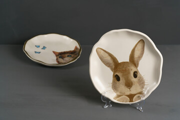 Two decorative plates featuring cat and rabbit illustrations, perfect for Easter-themed decor. Simple and colorful design on white plates, gray background, high resolution
