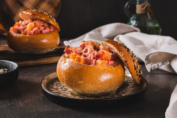 Close up of baked bun stuffed with sausage, tomatoes and cheese on a plate on the table
