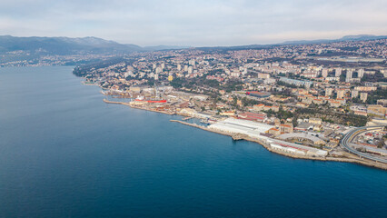 An aerial drone photo showcases ZTC Mall Rijeka along the stunning Adriatic coastline, capturing a breathtaking view of the cityscape. In the background, the newly developed Rijeka cargo terminal