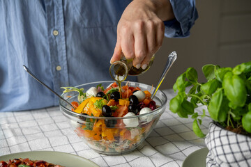 Women's hands mix salad with tomato tomato mozzarella vegetables and arugula in a large bowl for an easy diet lunch or dinner, a healthy balanced meal