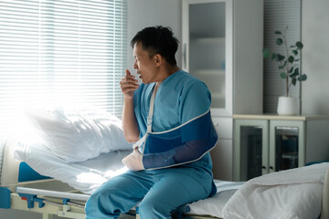 Asian patient wearing hospital gown, coughing and recovering from surgery, sitting on hospital bed...