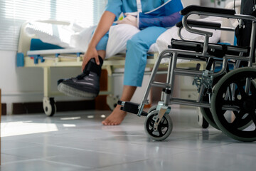 Patient recovering from injury, wearing cast and walking boot, sitting on hospital bed with...