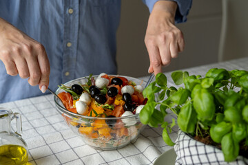 Women's hands mix salad with tomato tomato mozzarella vegetables and arugula in a large bowl for an easy diet lunch or dinner, a healthy balanced meal