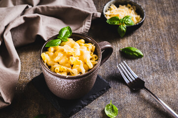 Cup with baked macaroni cheese and basil on the table