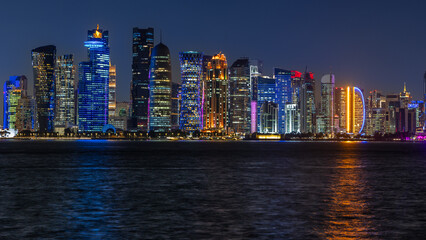 Naklejka premium Doha city business downtown center panorama illuminated at night, with modern skyscrapers and sea in the foreground, Qatar