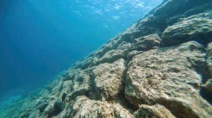 Fototapeta premium Underwater rocky slope, sunlight above, clear water, marine life background, ideal for travel brochures