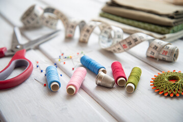 Sewing utensils - colored spools of thread, fabrics, tape measure and thimble on white wood