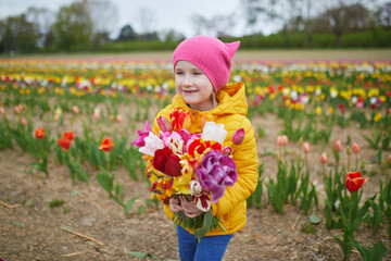 Adorable preschooler girl picking beautiful tulip flowers on farm. Outdoor summer activities for...