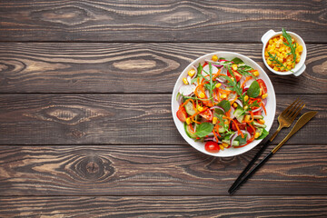 Fresh salad with vegetables. Arugula, spinach, cucumbers, tomato, onions carrots, corn andradishes in a plate on the table. Diet nutrition. Top view. Copy space