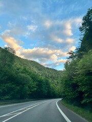 Fototapeta premium A winding road through lush green mountains under a blue sky with golden clouds, peaceful and scenic.