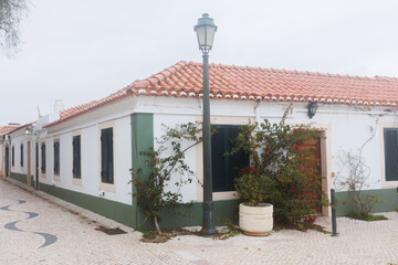 Charming narrow street paved with cobblestones, lined with traditional white houses with dark shutters and red-tiled roofs in Portugal. Stock photo