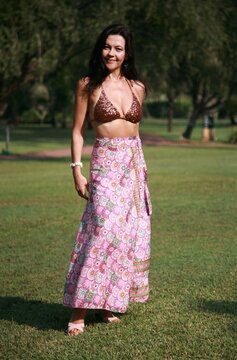 Smiling woman 51 years old in a silk Indian skirt and rhinestone bracelet with a white shell bracelet posing on a lawn with green grass