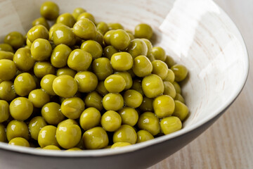 Canned organic green peas in a bowl close-up. Heap of wet marinated sweet peas in a white ramekin. Salad ingredient, vegetable protein and dietary fiber.