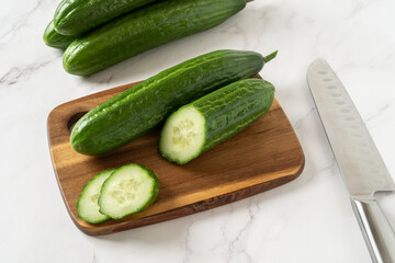 Cut in half cucumber on a wooden cutting board. Cooking vegetarian salad of green long cucumbers. Organic vegetables, healthy eating, harvest concept.