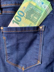 A crisp banknote is partially visible in the back pocket of blue denim jeans. The sunlight...