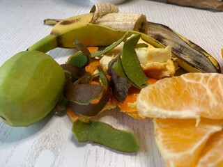 An assortment of fruit peels, including banana, orange, and apple, is displayed on a light wooden table, emphasizing the importance of composting and reducing food waste