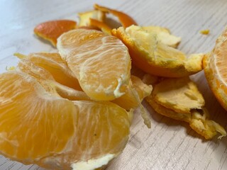 Juicy orange segments are partially peeled and spread out on a clean wooden surface. The vibrant orange color contrasts with the light wood, creating a refreshing snack setup