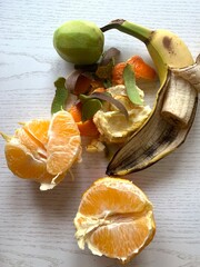 Fresh orange segments and various fruit peels are artistically arranged on a wooden surface, highlighting vibrant colors and natural textures illuminated by soft daylight
