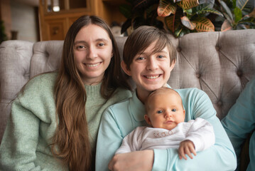 Fototapeta premium Smiling siblings, two teenagers and a baby. Brother holding younger brother and sitting next to older sister.