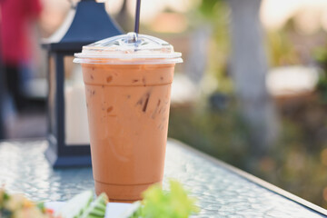 a plastic cup filled with an iced beverage, likely iced coffee or tea, with a clear plastic lid and a black straw.