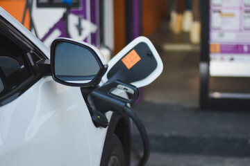 electric vehicle (EV) being charged. The focus is on the side mirror of the white car and the charging port where the charging cable is connected.