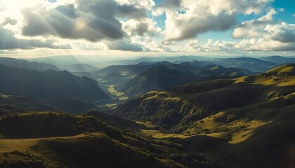 Fototapeta premium Stunning Aerial View of Rolling Green Mountains and Valleys Under a Dramatic Cloudy Sky with Sunbeams