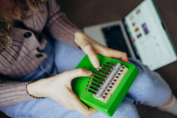Woman playing a vibrant green kalimba while engaging in an online course on her laptop, immersing herself in the joy of learning and exploring a new musical hobby